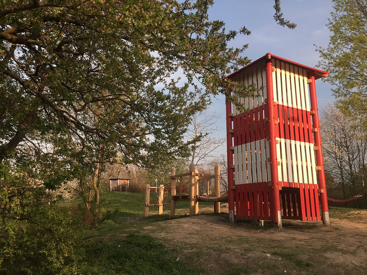 Piratenspielplatz Park, rot-weiß gestreifter Holzturm, aus dem eine Holzbrücke führt.
