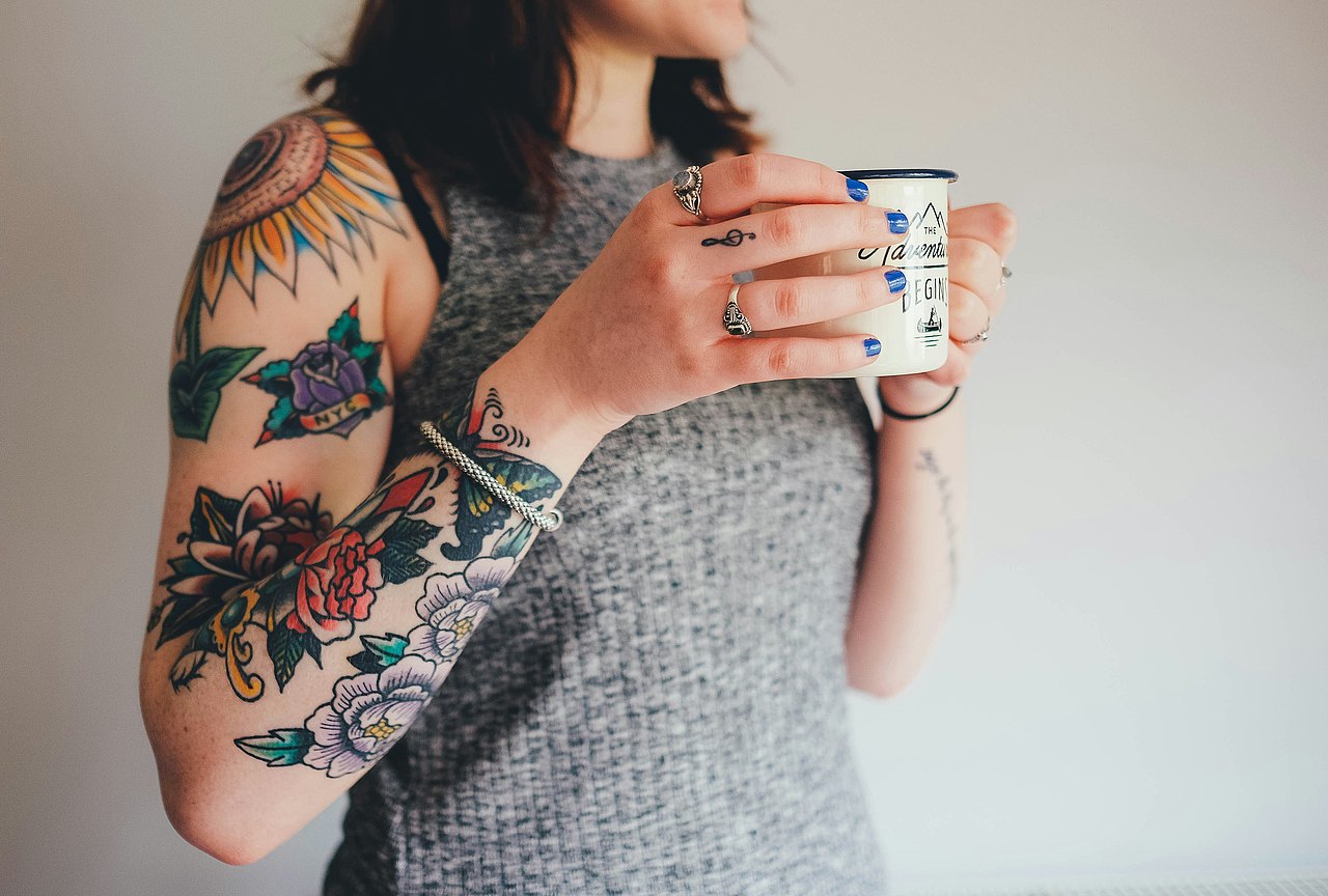 Eine tätowierte Person hält eine Tasse in der Hand. 