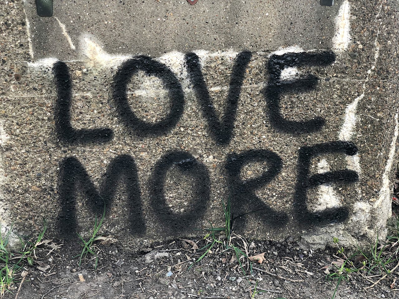 Graffiti grau mit schwarzer Schrift "Love More"