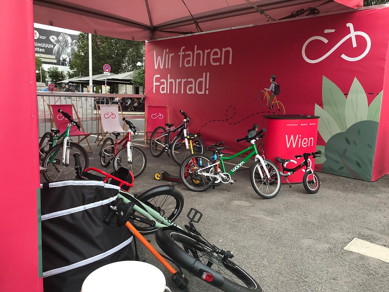 Eine rosa Überdachung von der Mobilitätsagentur mit der Aufschrift "Wir fahren Fahrrad!". Darunter stehen mehrere Fahrräder und drei Liegestühle.
