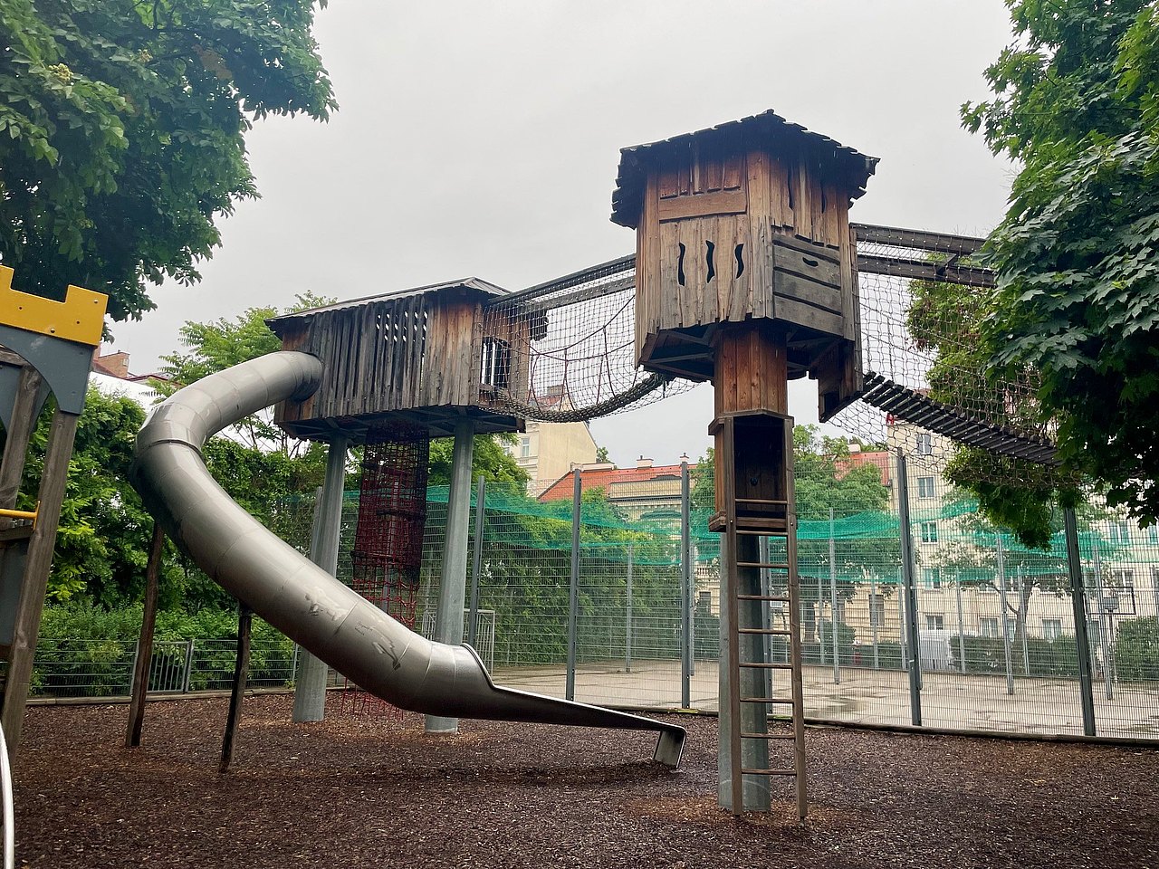 2 hohe Hloztürme die mit einem Kletternetztunnel verbunden sind, mit einer langen Rutsche