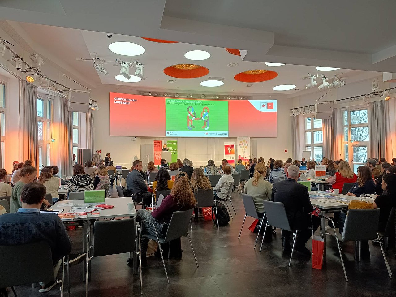 Veranstaltungssaal im Arbeiterkammer-Bildungszentrum: Besucher*innen an Infotischen