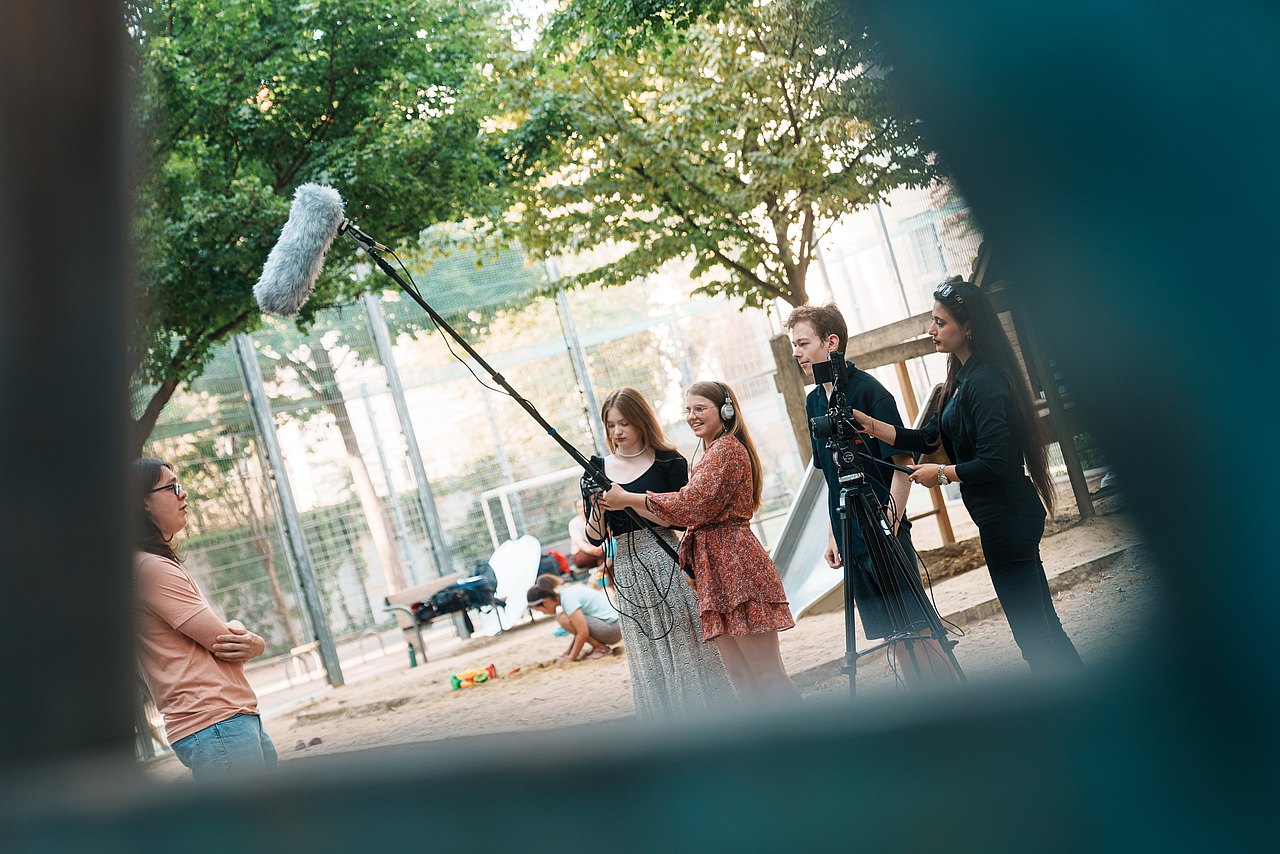 Mehrere Jugendliche filmen ein Interview in einem Park.