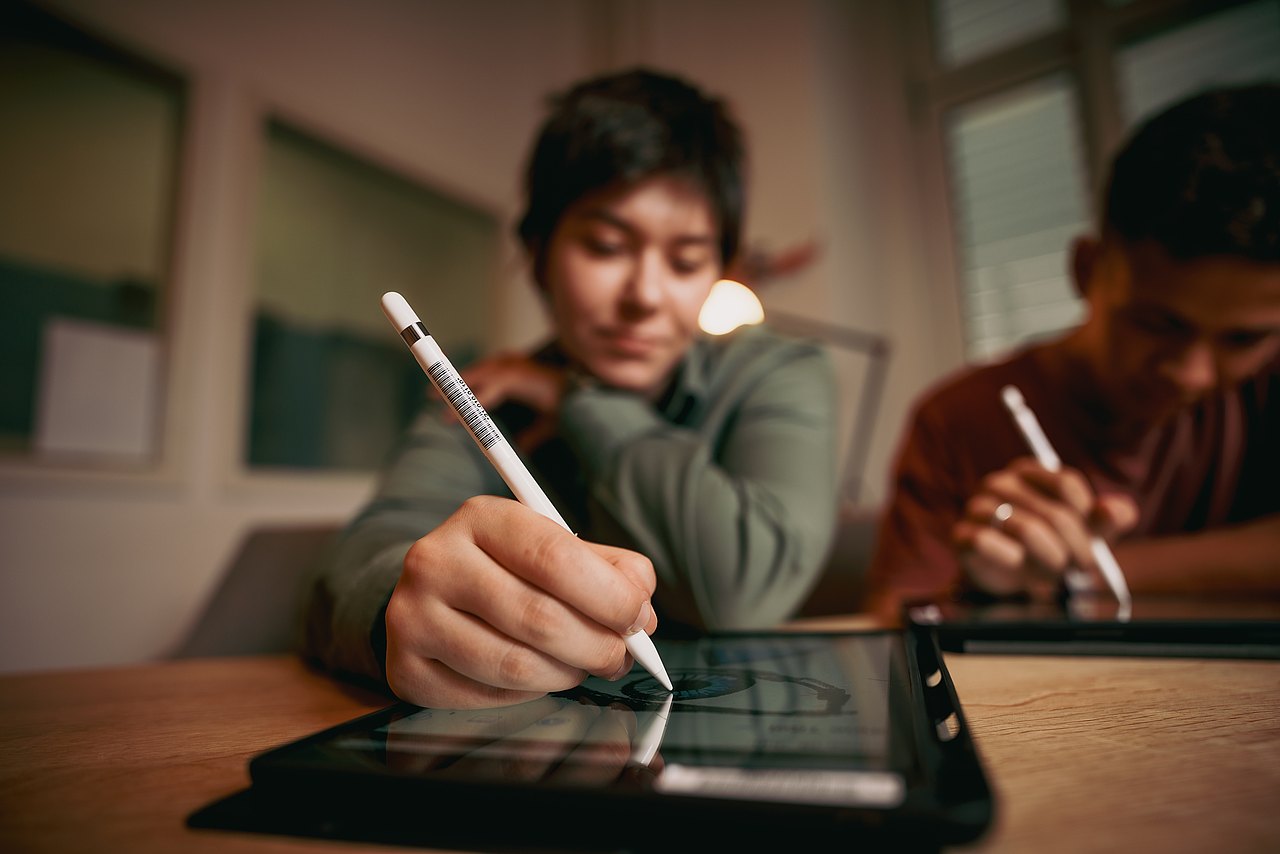 Zwei Jugendliche sitzen an einem Tisch und malen mit Stiften auf iPads.