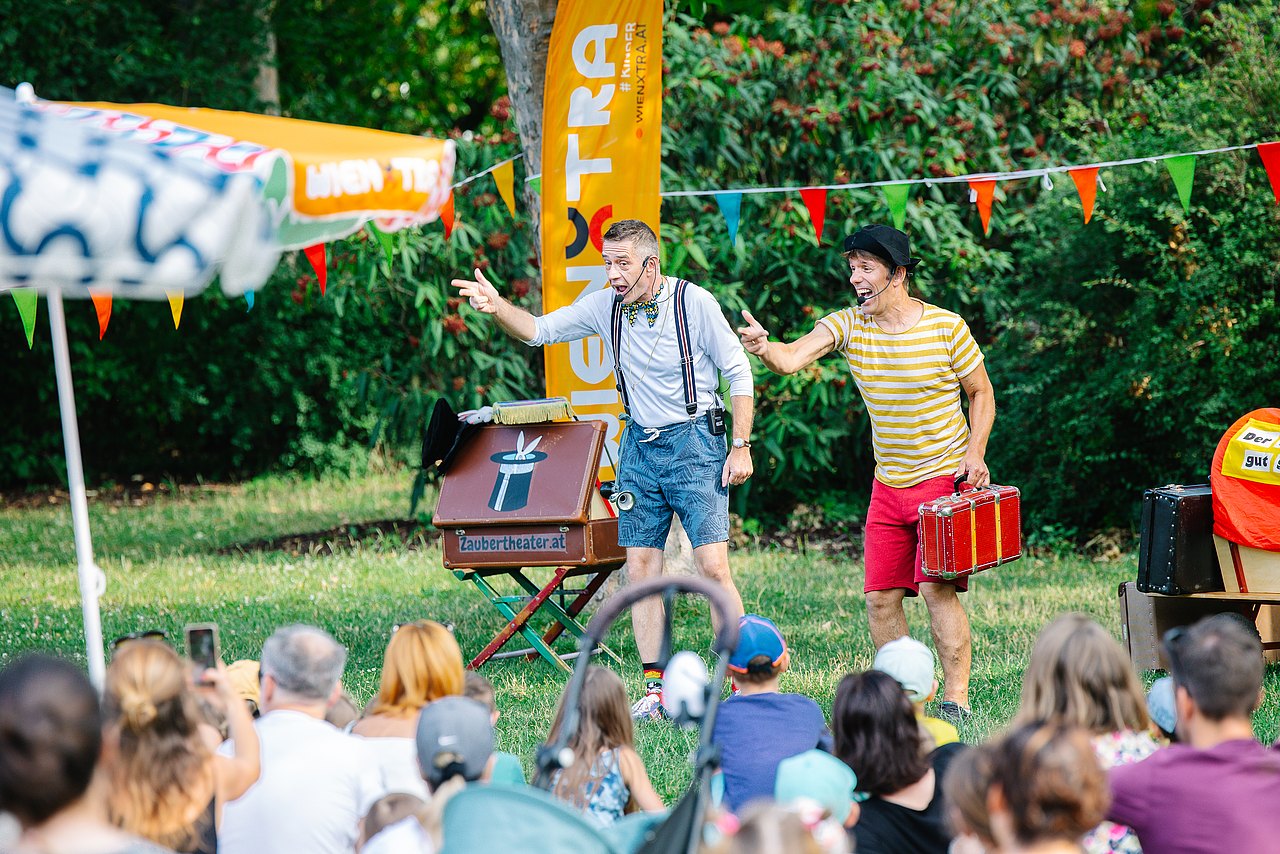 Zwei Clowns treten im Park direkt auf der Wiese auf,  Kinder und Familien schauen zu