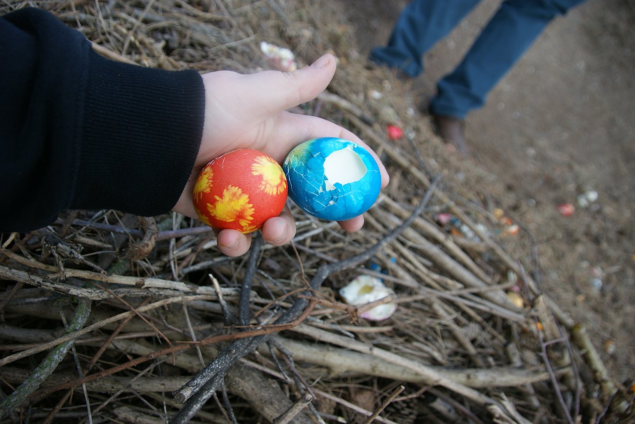 Eine Hand hält zwei bunte Eier. Eines ist heil, das andere ist stark zerdrückt, die Schale hat ein großes Loch.