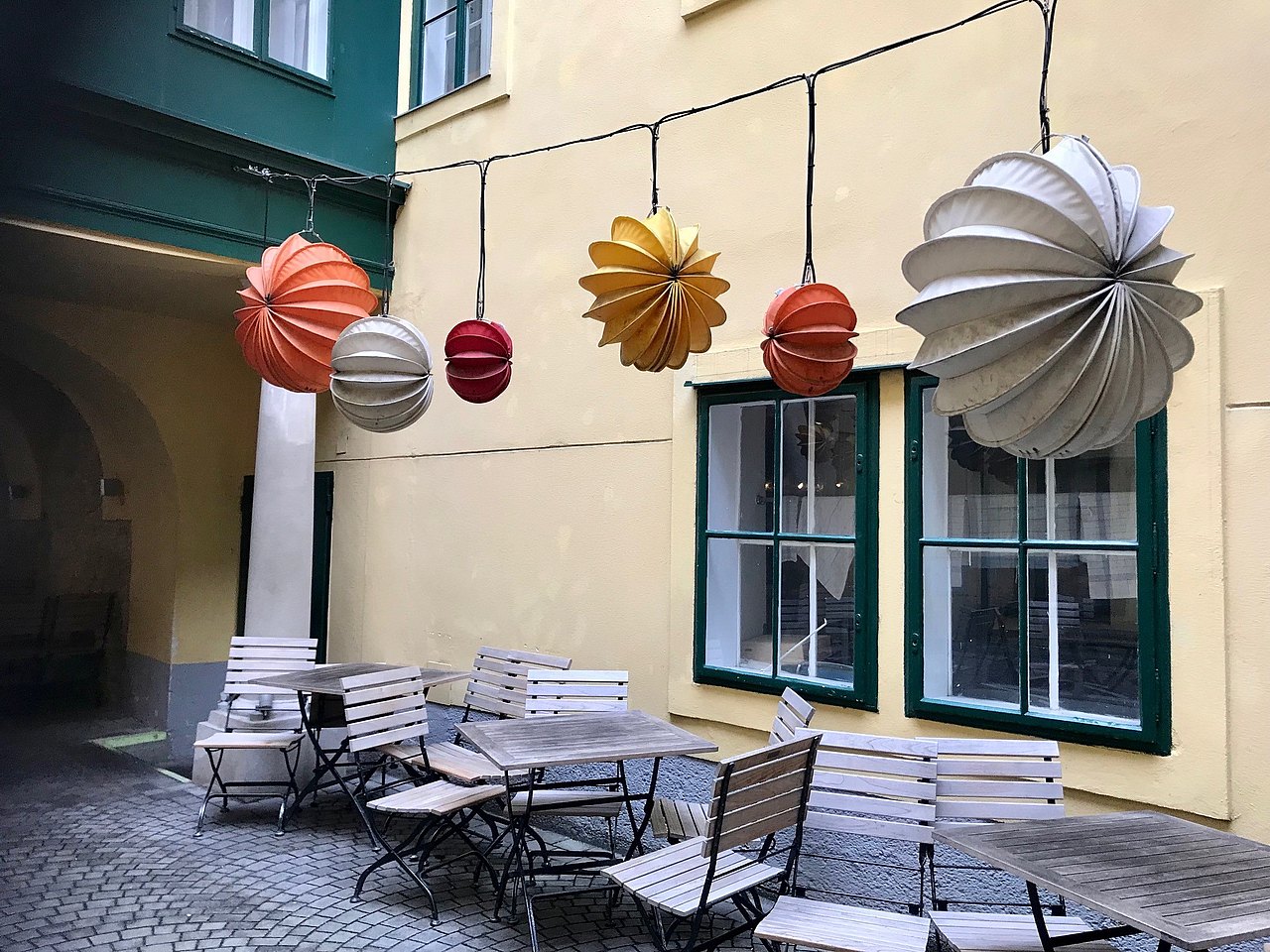 Innenhof mit Tischen und Sesseln darüber hängen viele bunte Lampions