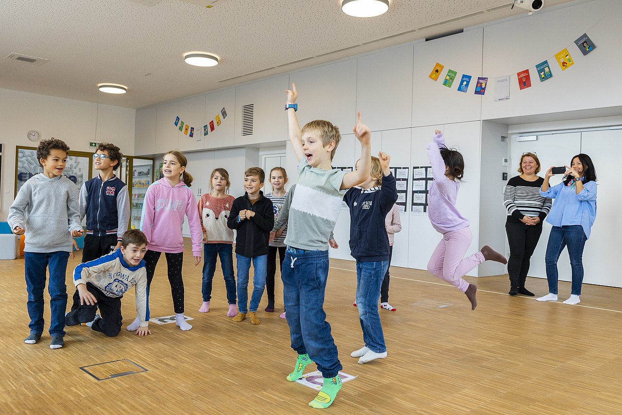 221117_2-4 Kinder stehen und freuen sich, Kind in der Mitte springt vor Freude in die Luft