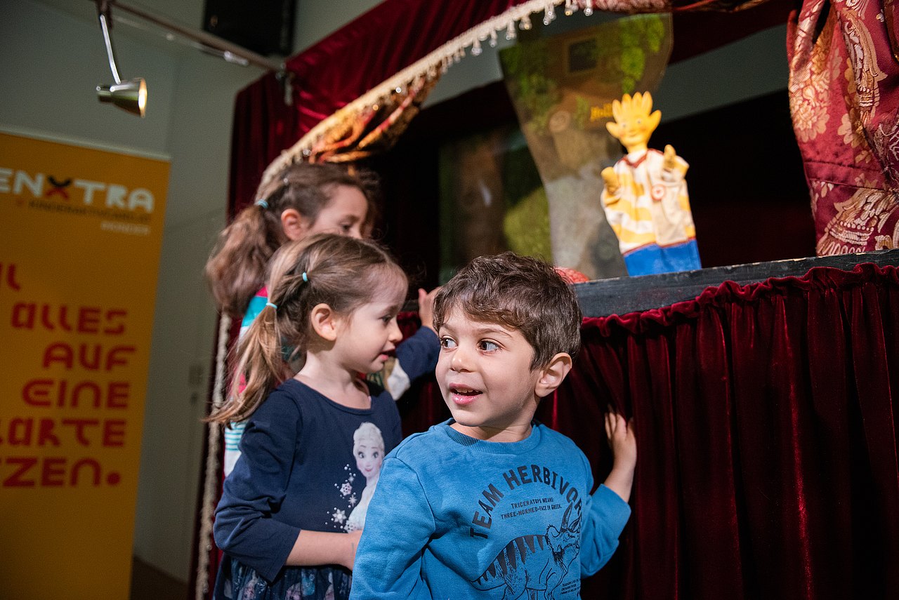 Kinder stehen vor einer Puppentheaterbühne mit Holli-Puppe