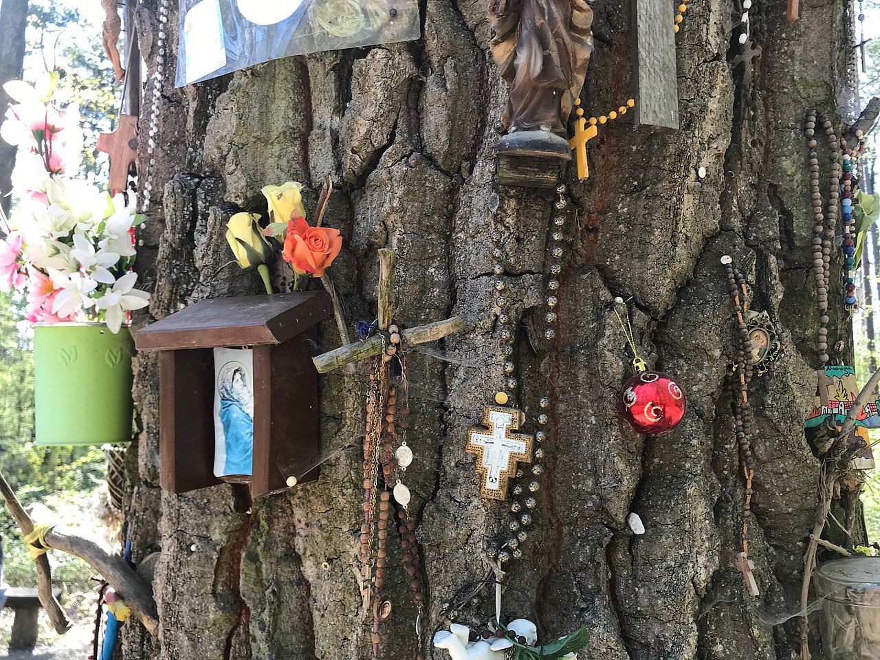 Baumstamm mit Kreuzen, Rosenkränzen und Heiligenbild sowie Christbaumkugel