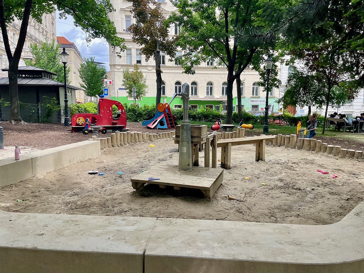 Sandkiste Im Vordergrund Sandkiste mit Spielgeräten, im Hintergrund rotes Spielauto