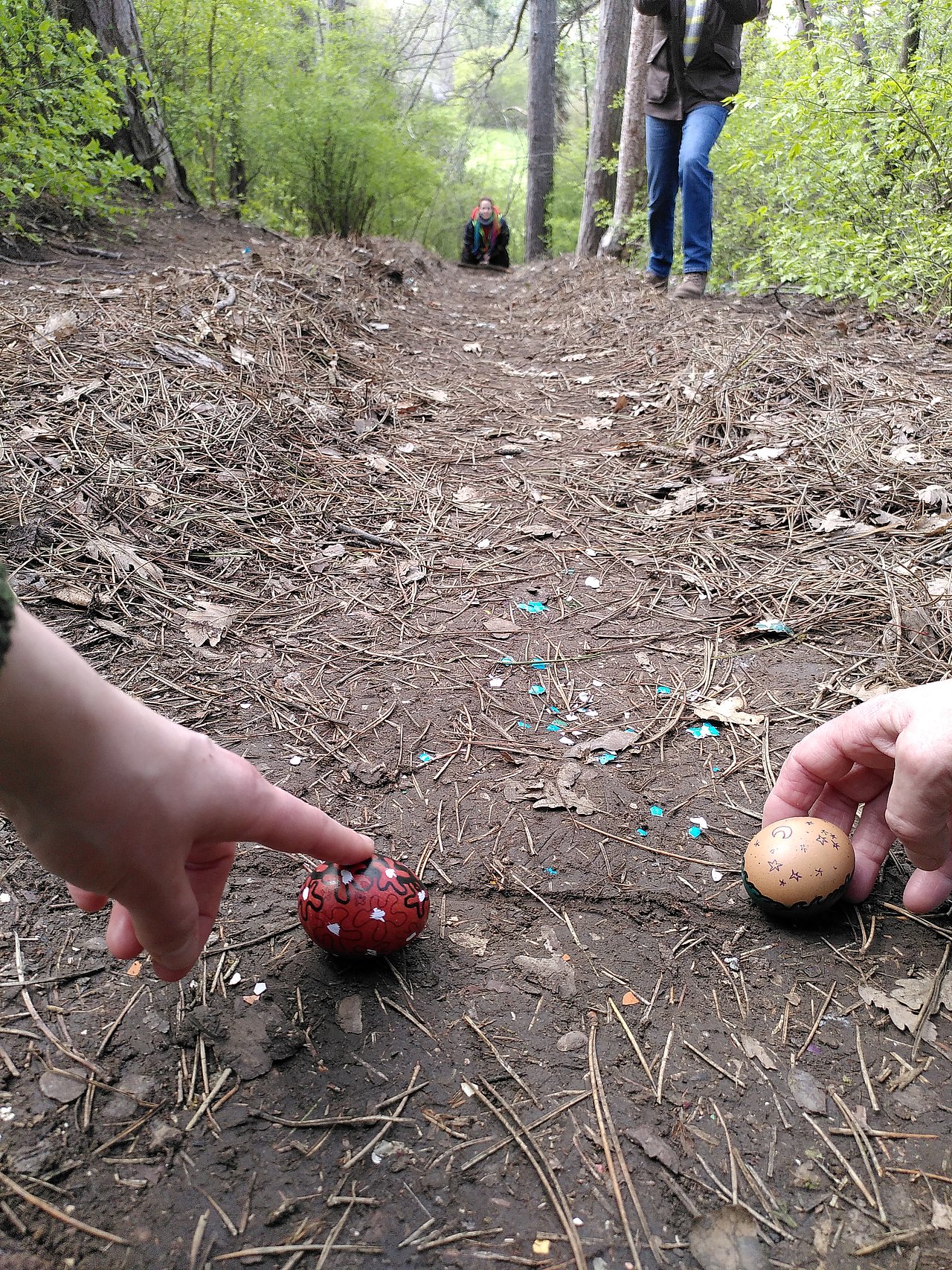 Zwei Hände halten zwei bunte Eier vor einem Erdhügel fest, damit sie noch nicht runter rollen.
