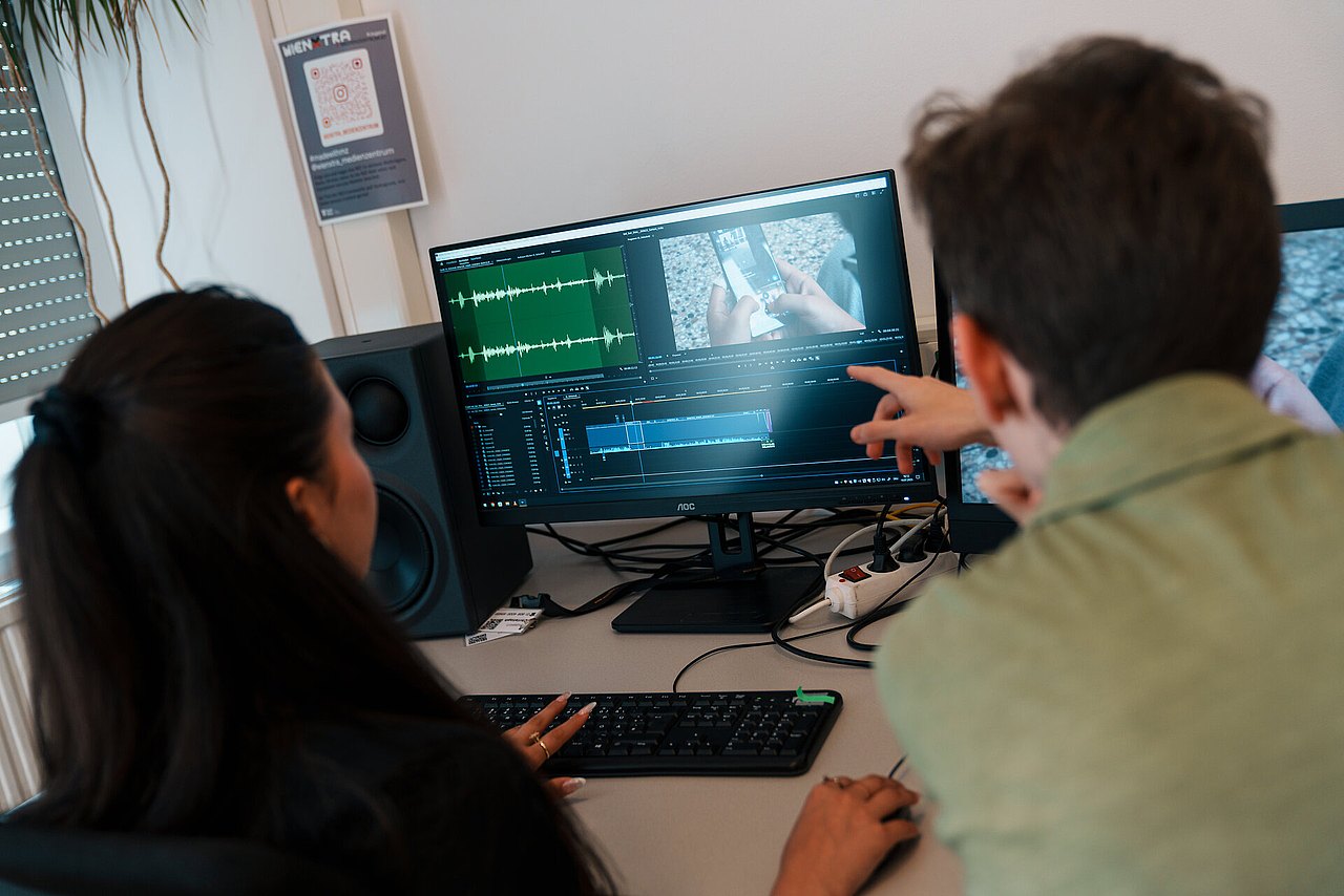 Zwei Jugendliche schneiden einen Film auf einem Computer-Monitor.