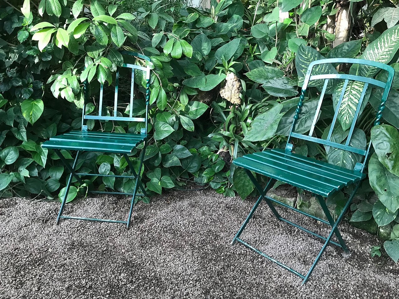 grüne Metallstühle vor tropischen Pflanzen