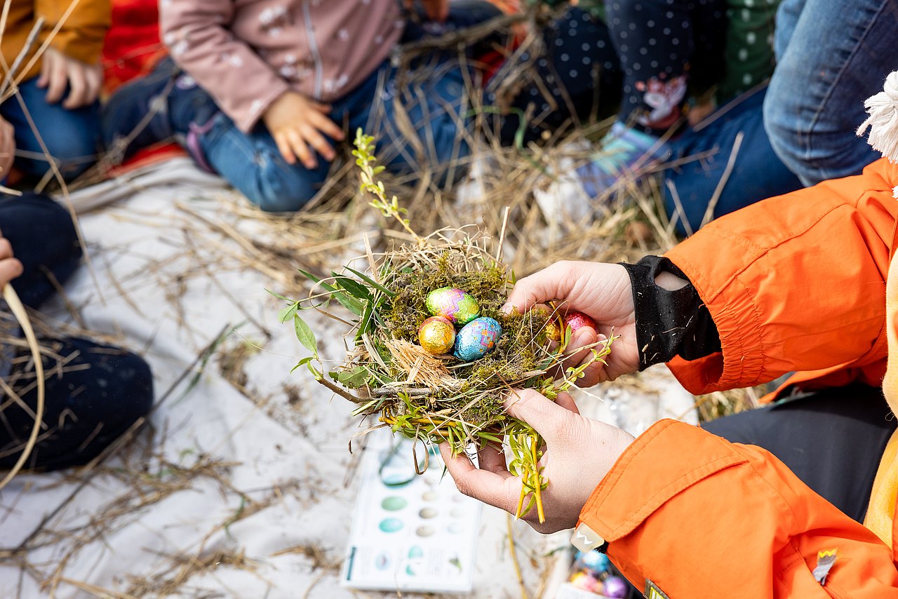Kind hält ein Osternest mit drei kleinen Ostereiern in der Hand