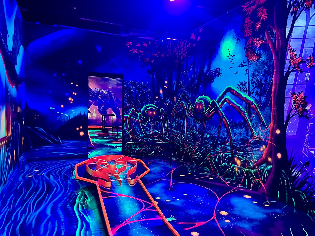 abgedunkelter Raum mti Neonfarbenen Bildern, große Spinne im Hintergrund auf die Wand gemalt