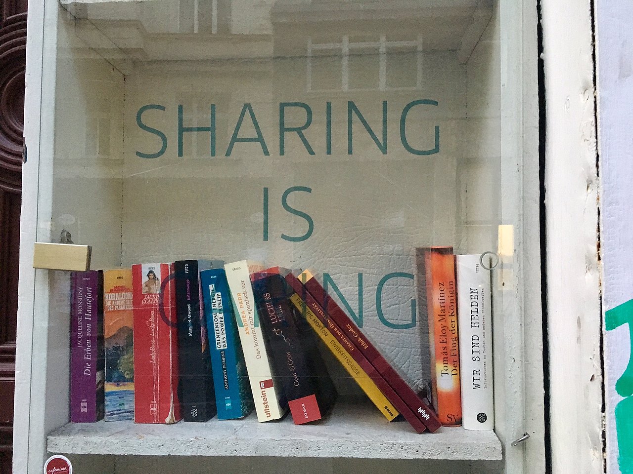 Sharing is Caring Bücherschrank mit dem Text Sharing is Caring auf der Glastüre