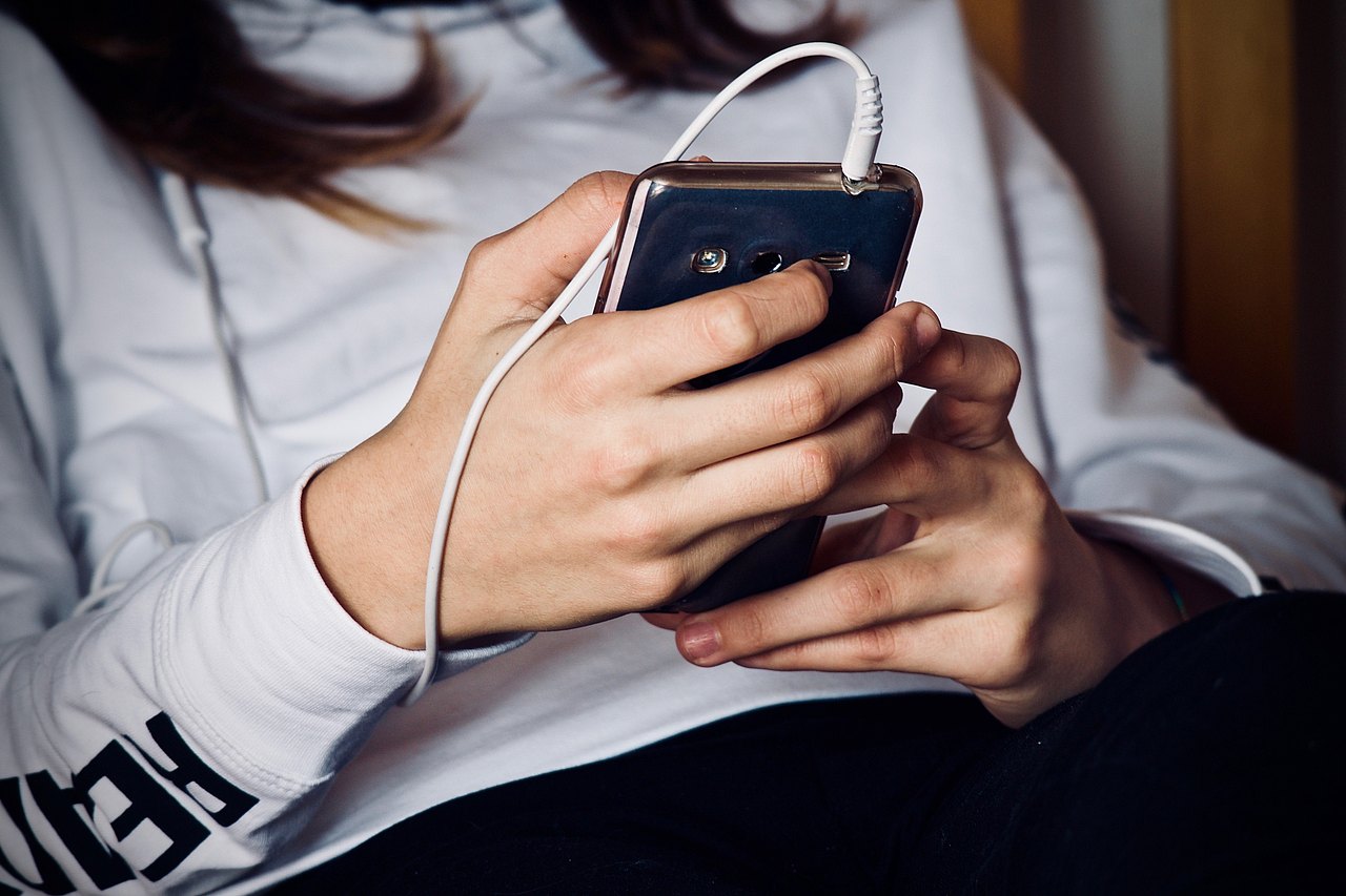 junger Mensch von dem man nur die Hande mit einem Smartphon und Kophörerkabeln sieht