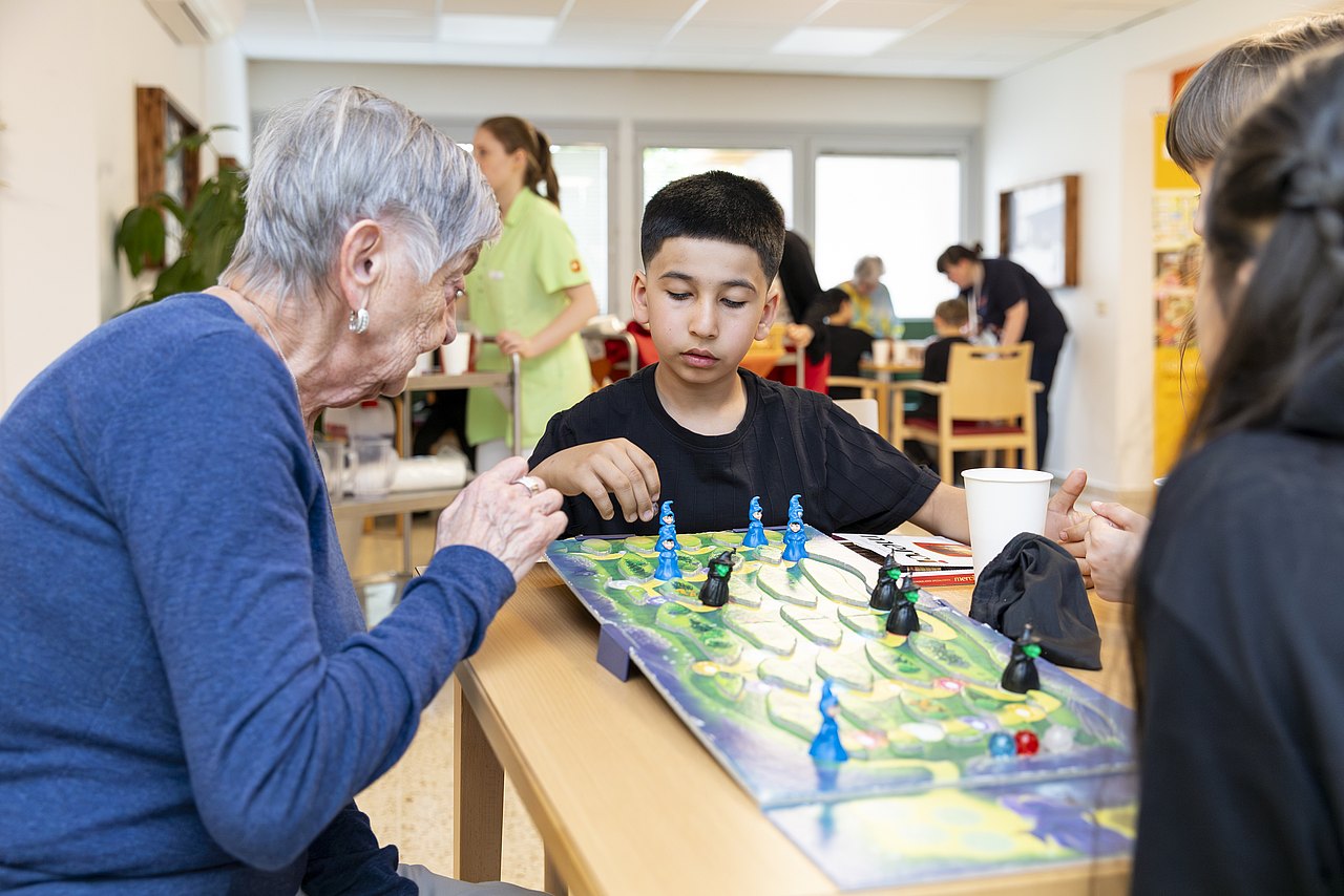Bezirksjugendsingen 2024 Kinder spielen ein Brettspiel mit Pflegeheimbewohner*innen