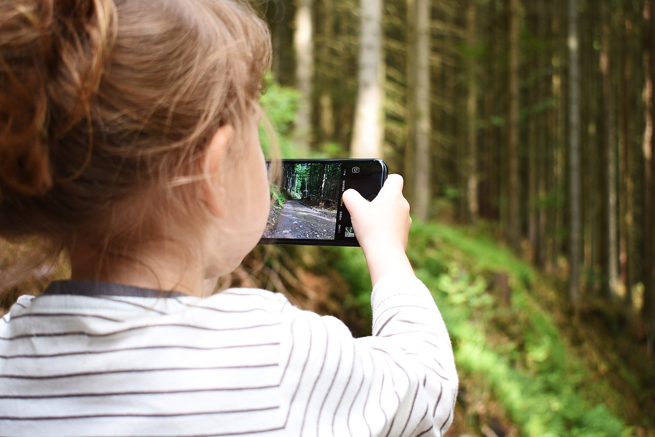 Kind mit Handy im Wald Kind, das mit einem Handy im Wald filmt, von hinten aufgenommen