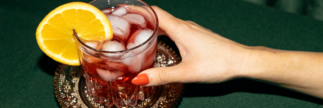 Eine Hand greift nach einem Getränk mit Zitronenscheibe auf einem Tisch – Symbolbild zum Thema K.o.-Tropfen.