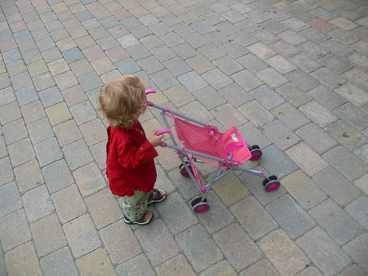 Kleinkind mit Puppenwagen Kleinkind von hinten seitlich mit Puppenwagen