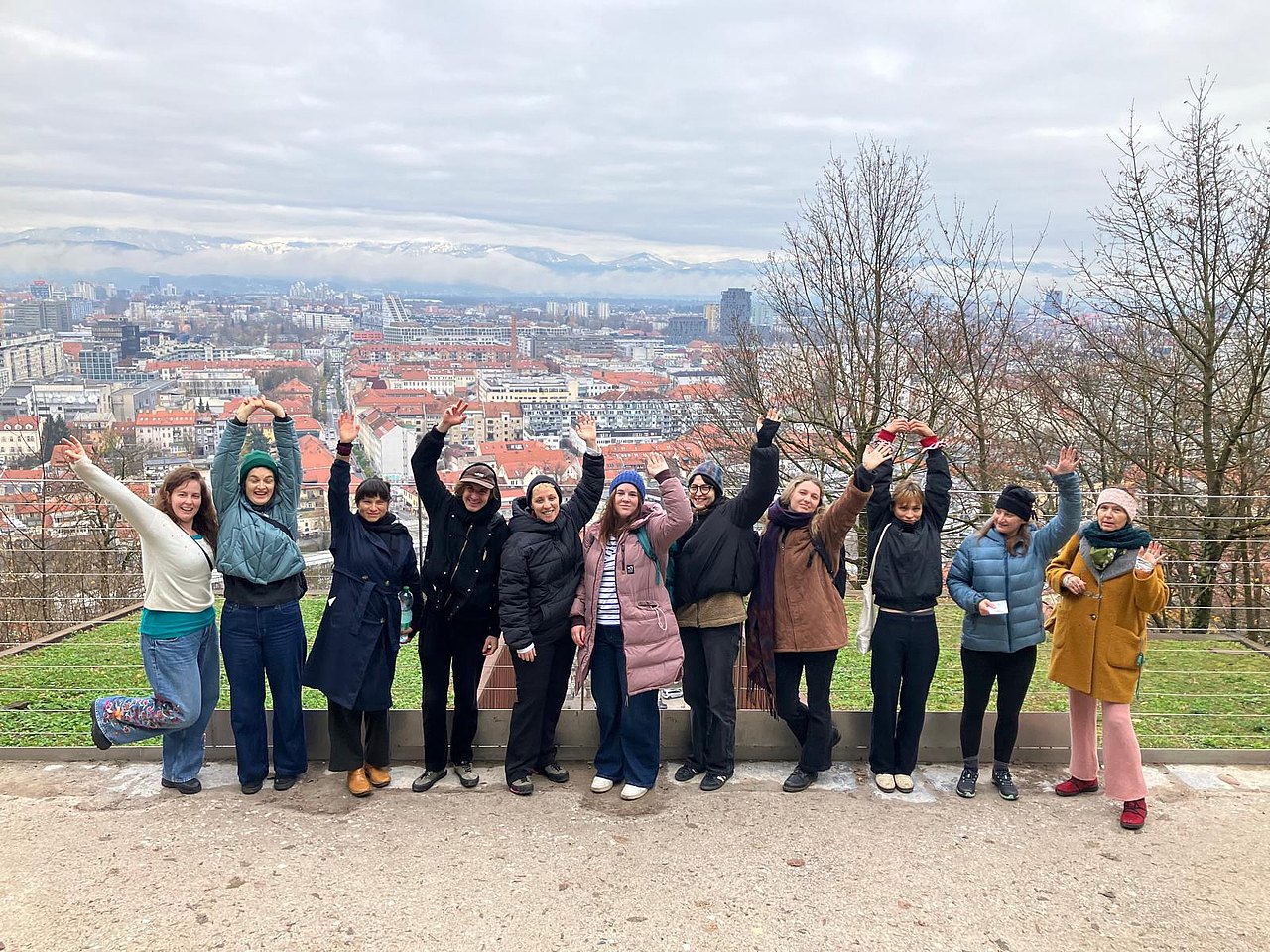 Eine Gruppe von 10 Personen in Winterkleidung steht vor einem Panorama der Stadt Ljubljana. Alle Personen strecken die Hände in die Luft.