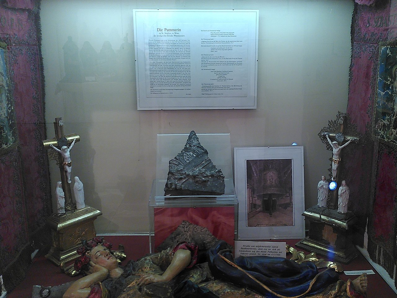 Ein Stück der Pummerin in einem Schaukasten, umgeben von christlichen Symbolen.