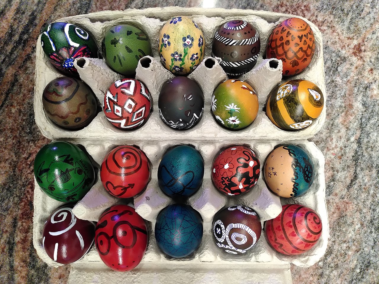 Ein Eierkarton voll gefüllt mit bunten, verschieden bemalten Eiern.