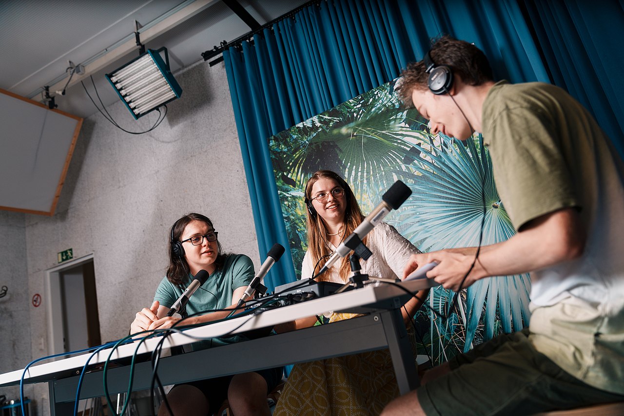 Drei Jugendliche sitzen an einem Tisch und nehmen einen Podcast auf.