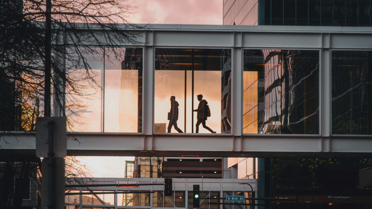 zwei Personen gehen in einem Geschäftsgebäude über eine Brücke 