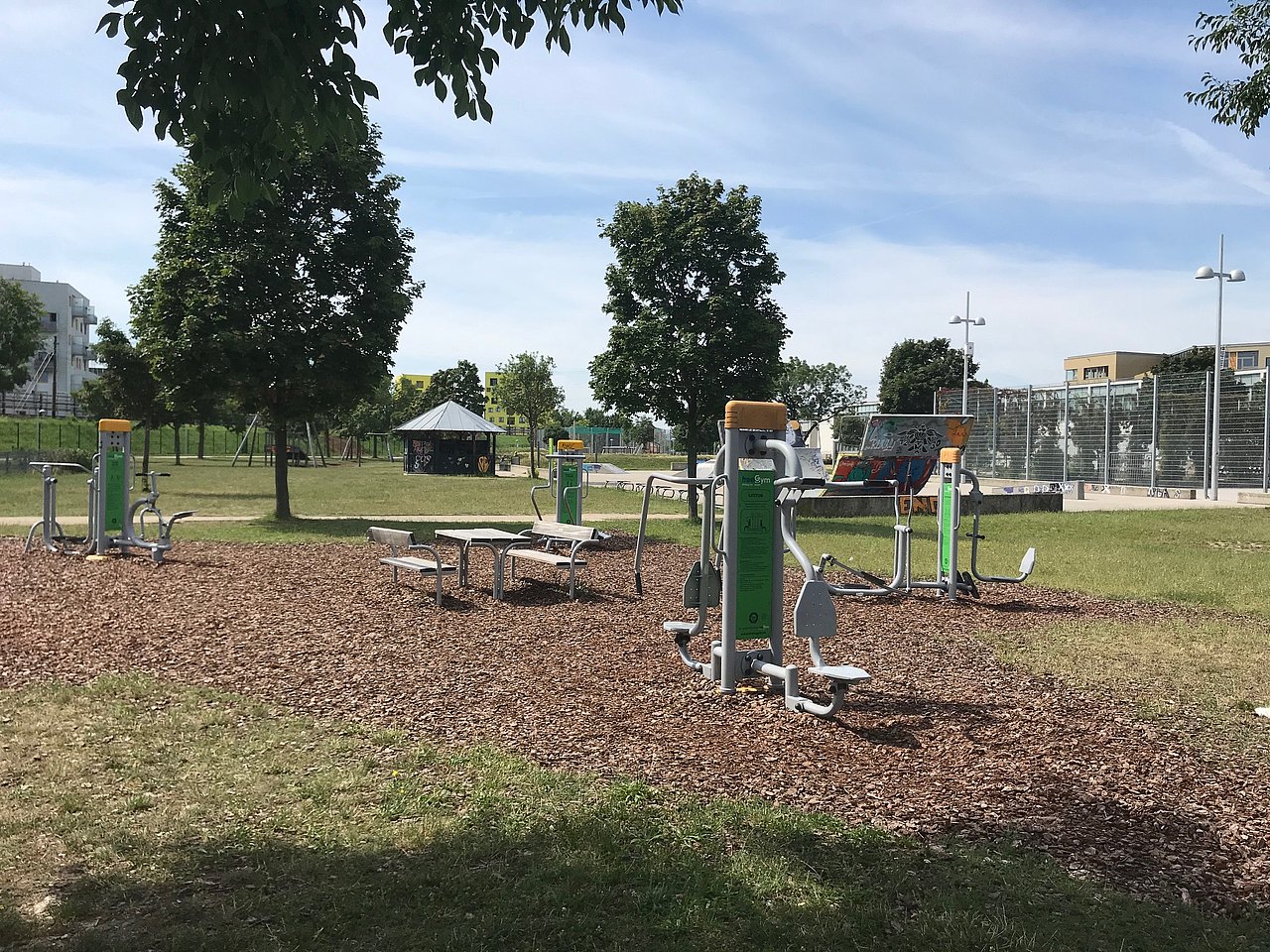 Fitness-Geräte auf Rindenmulch mit Wiese und Bäumen