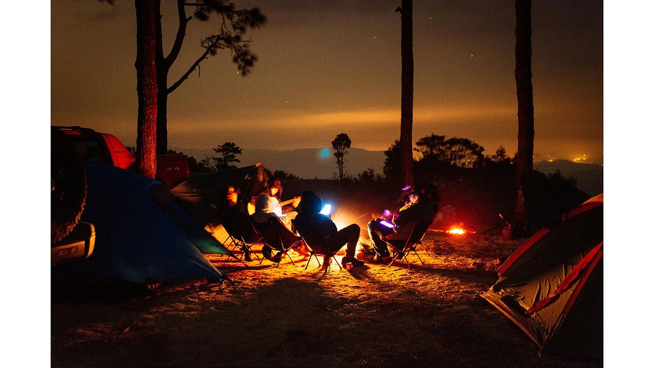 Ein Wald in Abenddämmerung mit Personen die in Zelten übernachten