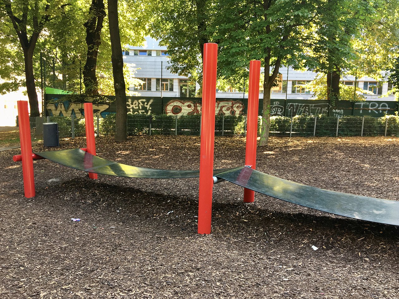 Bereich bedeckt mit Rindenmulch. In der Mitte ein langer breiter Gummistreifen auf 6 roten Pfosten.