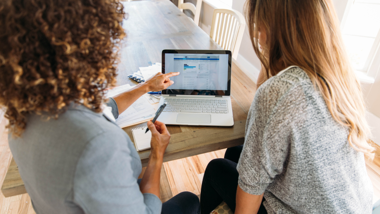eine Person zeigt der anderen Person eine Finanzaufstellung am Laptop