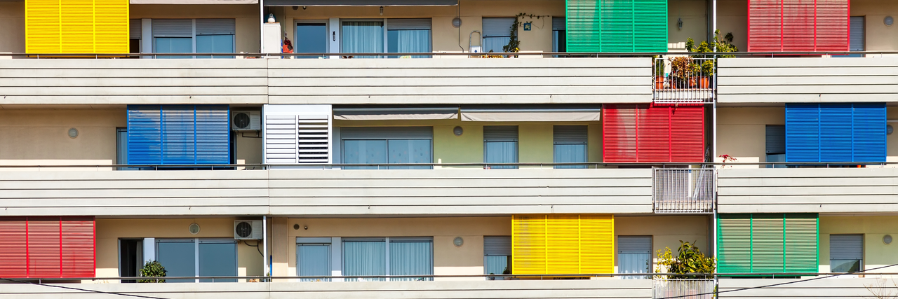 eine Reihe an Wohnungen mit Balkonen mit buntem Sonnenschutz