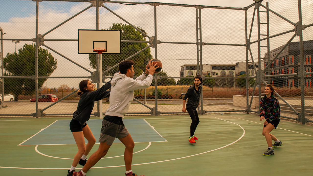 Fünf Personen spielen auf einem Outdoor-Basketballplatz Basketball.