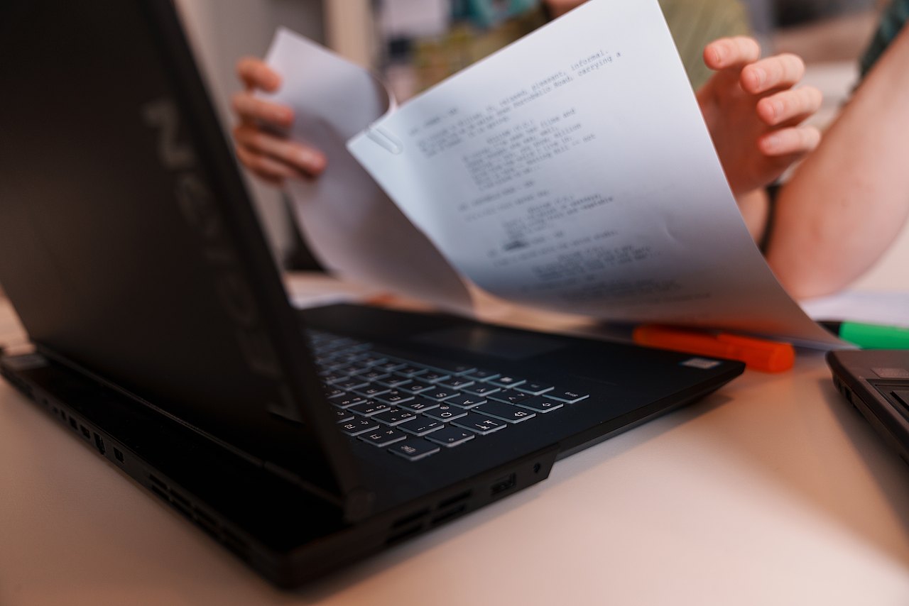 Mehrere Personen sitzen an einem Tisch und besprechen gemeinsam Unterlagen. Eine Person zeigt auf ein Dokument neben einem aufgeklappten Laptop.