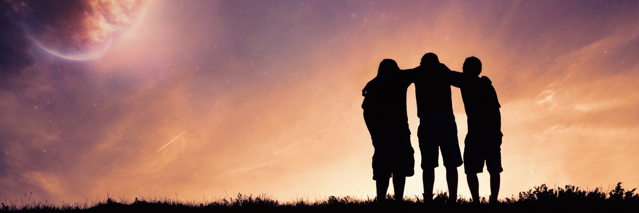 drei Freund*innen stehen auf einer Wiese und legen gegenseitig die Arme um die Schultern