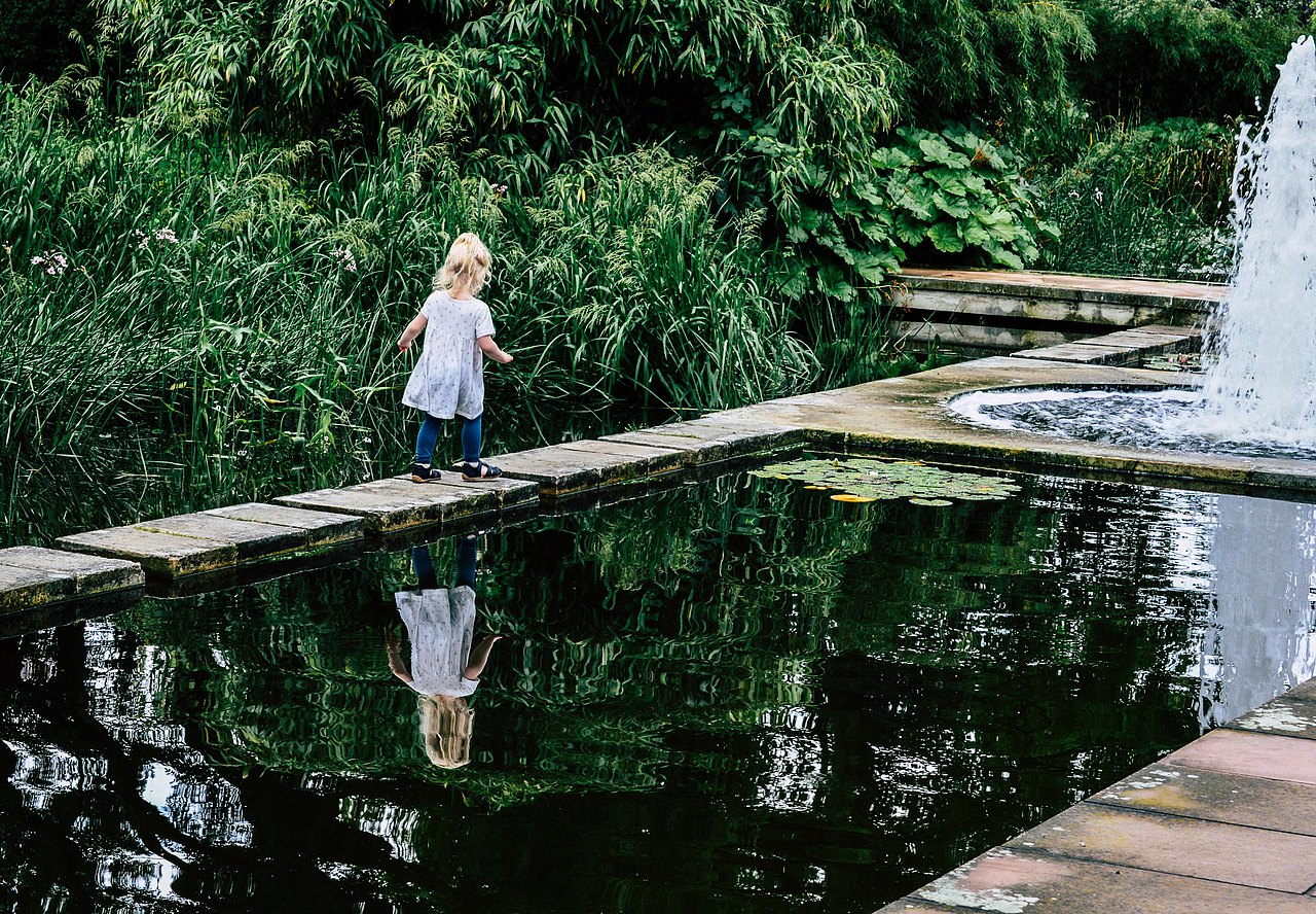 Kind auf Steg kleines Kind auf einem schmalen Holzsteg, der über einen ruhigen Teich führt