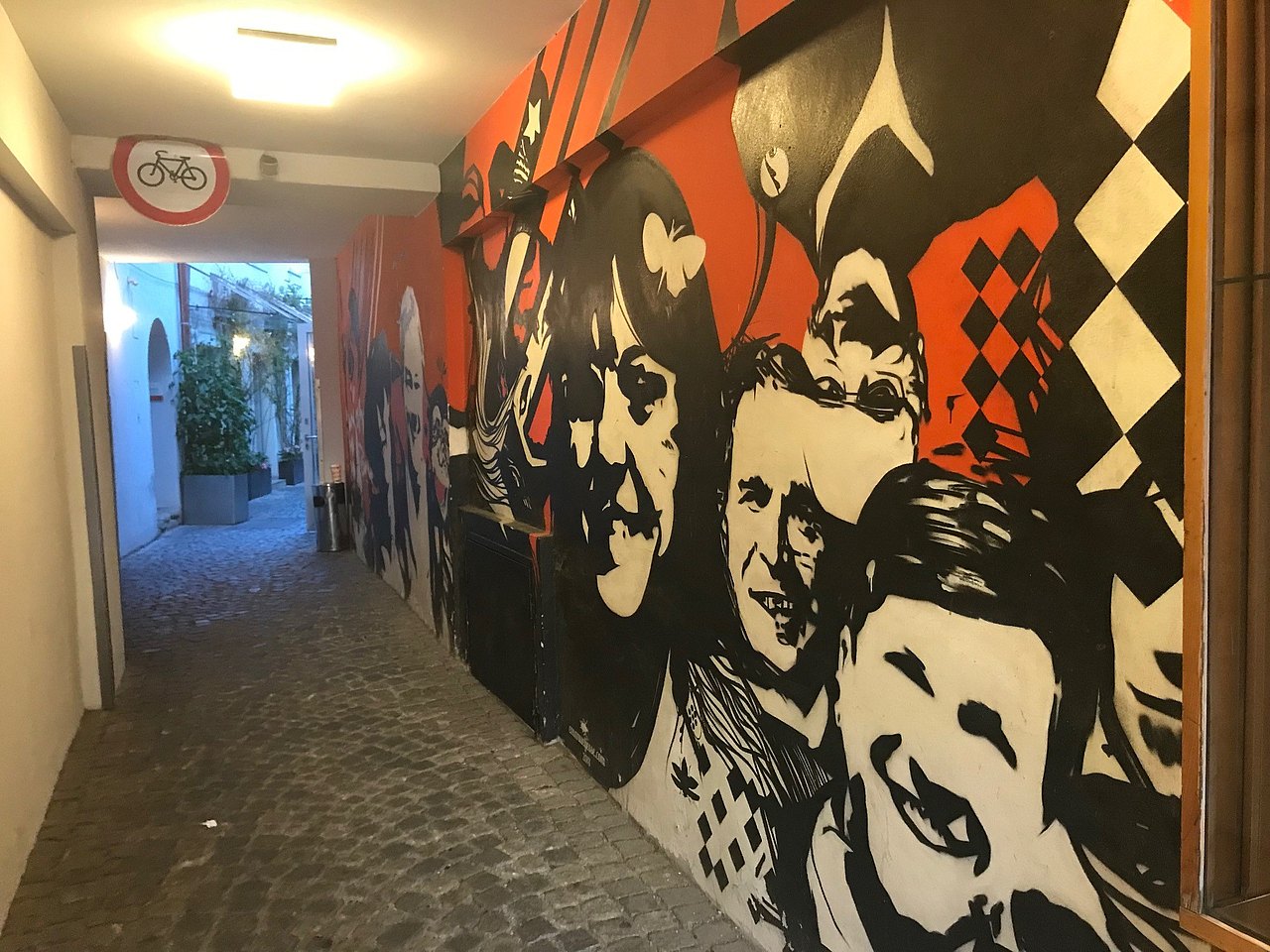 Gang, auf der rechten Seite Grafitti mit vielen unterschiedlichen Gesichtern in Schwarz-Weiß auf rotem Grund  vom Küstler Emanuel Jesse 