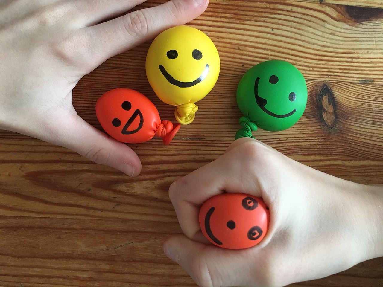 Antis Stress Bälle Kinderhand quetscht kleine bunte Bälle auf welche Gesichter gemalt wurden