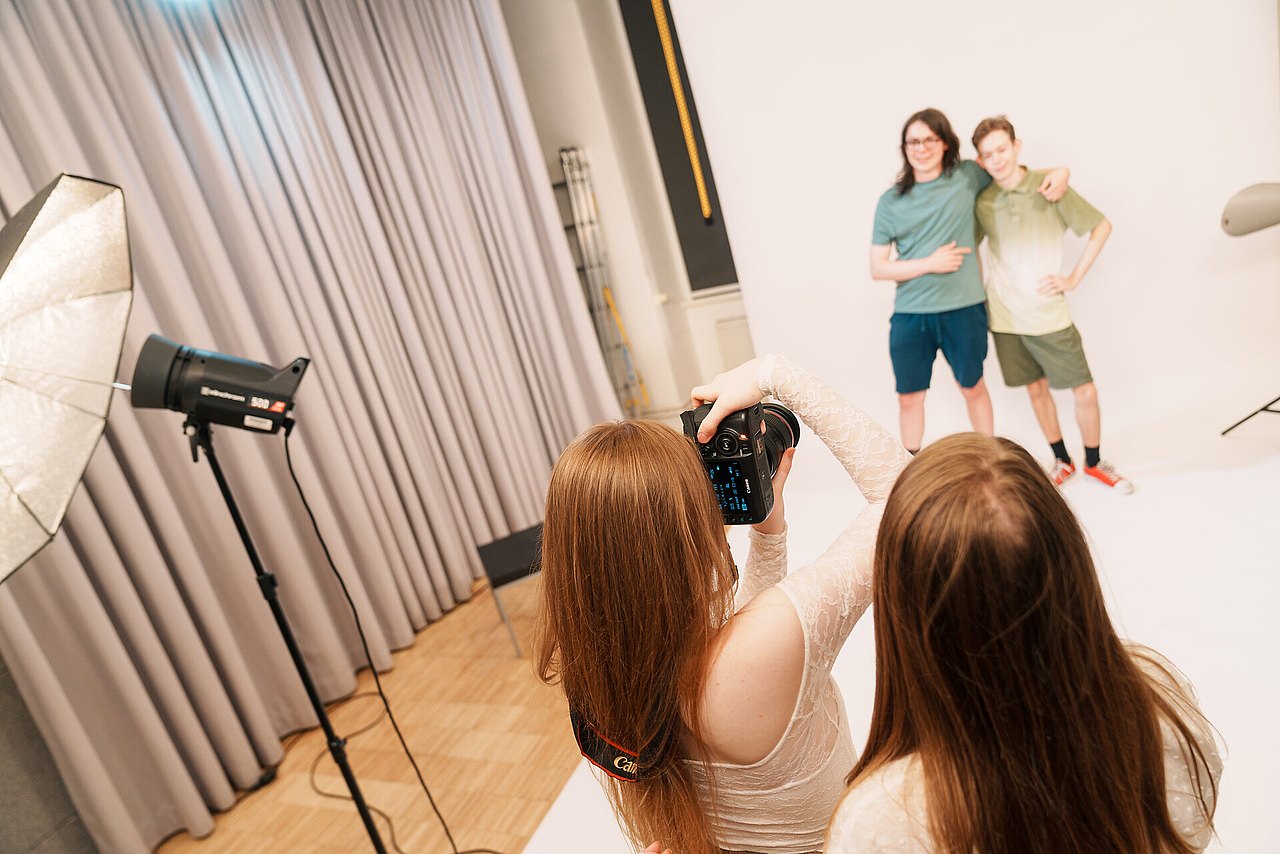 Zwei Jugendliche werden von zwei anderen Jugendlichen vor weißem Hintergrund in einem Studio fotografiert.