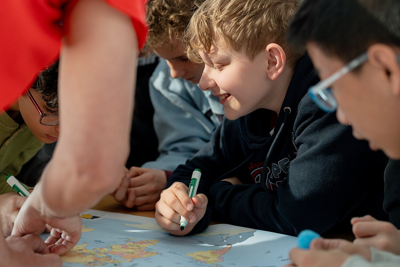 Kinder mit Stiften zeichnen auf einer Weltkarte