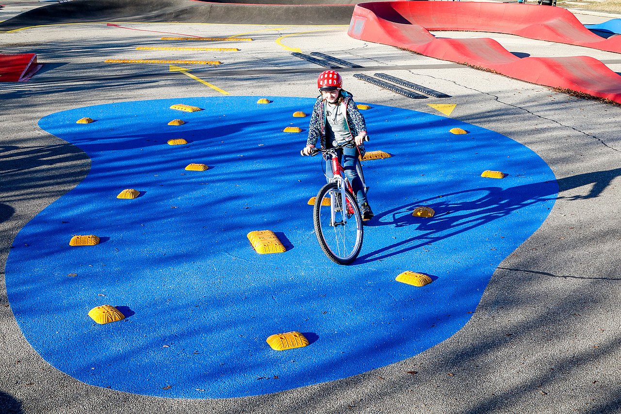 Radmotorikpark Ein Kind fährt mit Fahrrad über eine blaue Fläche mit kleinen Hindernissen.