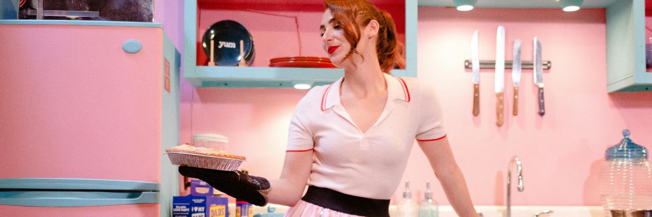 Eine Frau steht in einer rosa Küche und hält einen gebackenen Kuchen