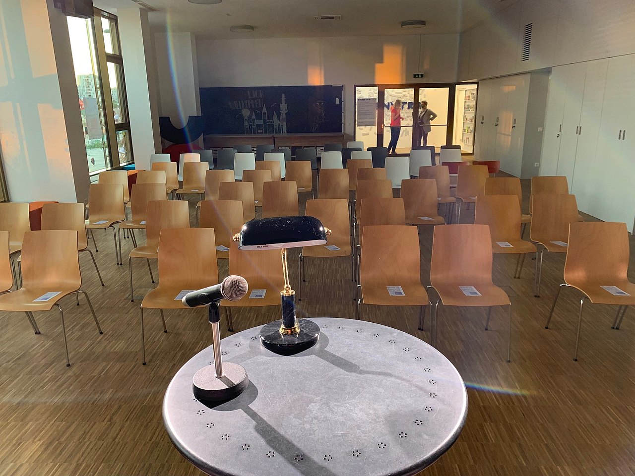 Raum mit Bestuhlung, Sicht von Bühne mit Tisch und Mikrofon