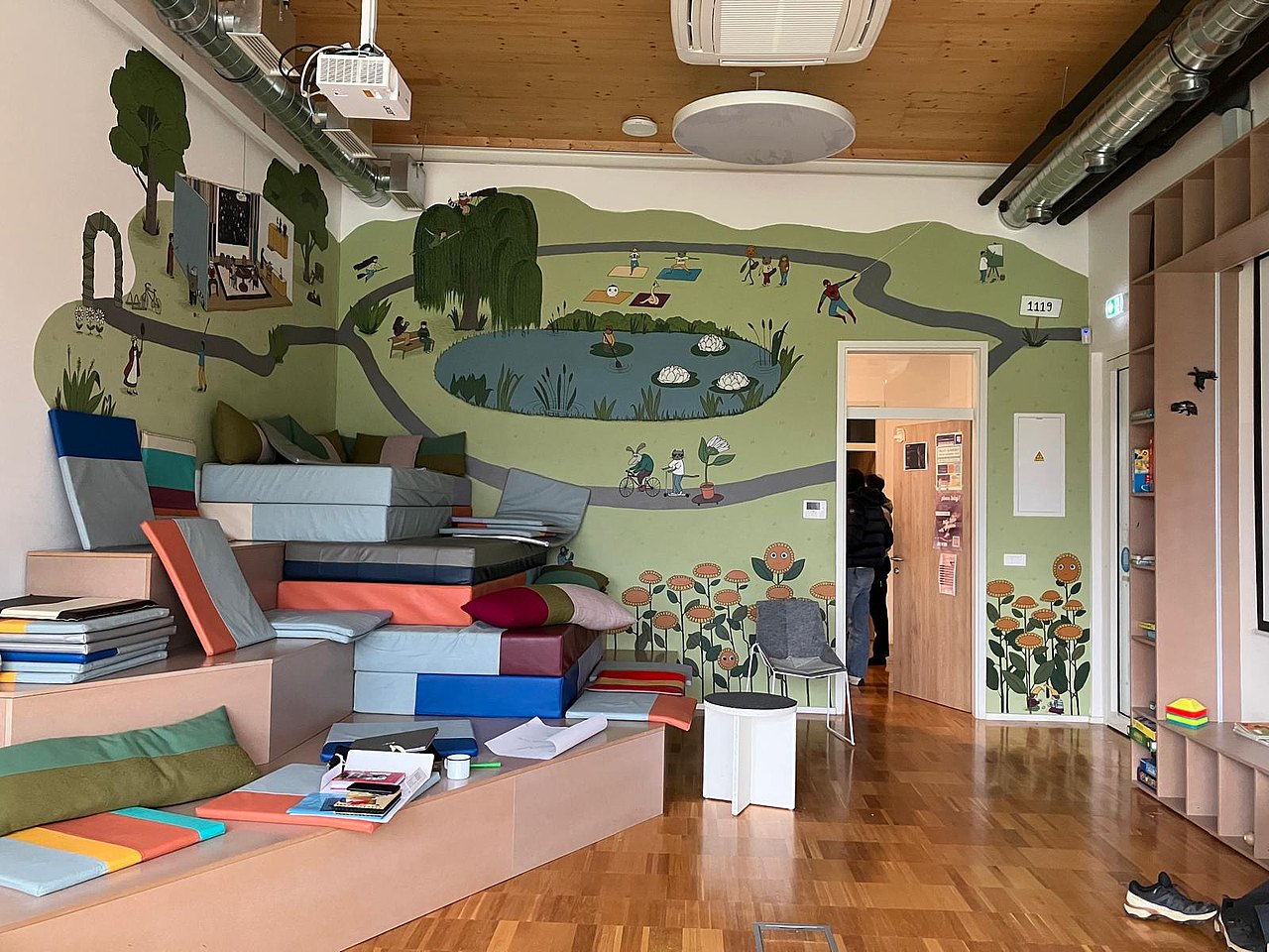 Zu sehen ist ein Raum mit aufgemalter Landschaft auf der Wand und bequemen Sitzmöglichkeiten, in Form von Treppenstufen.