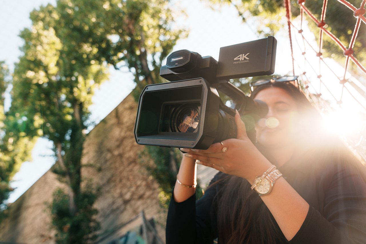 Eine Jugendliche filmt mit einer Panasonic-Videokamera in einem Park.
