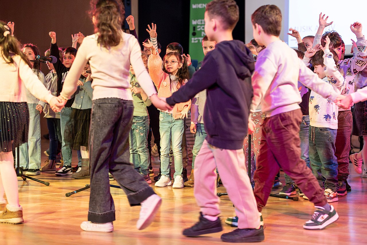 Kinder halten sich an den Händen und bewegen sich im Kreis zu Musik